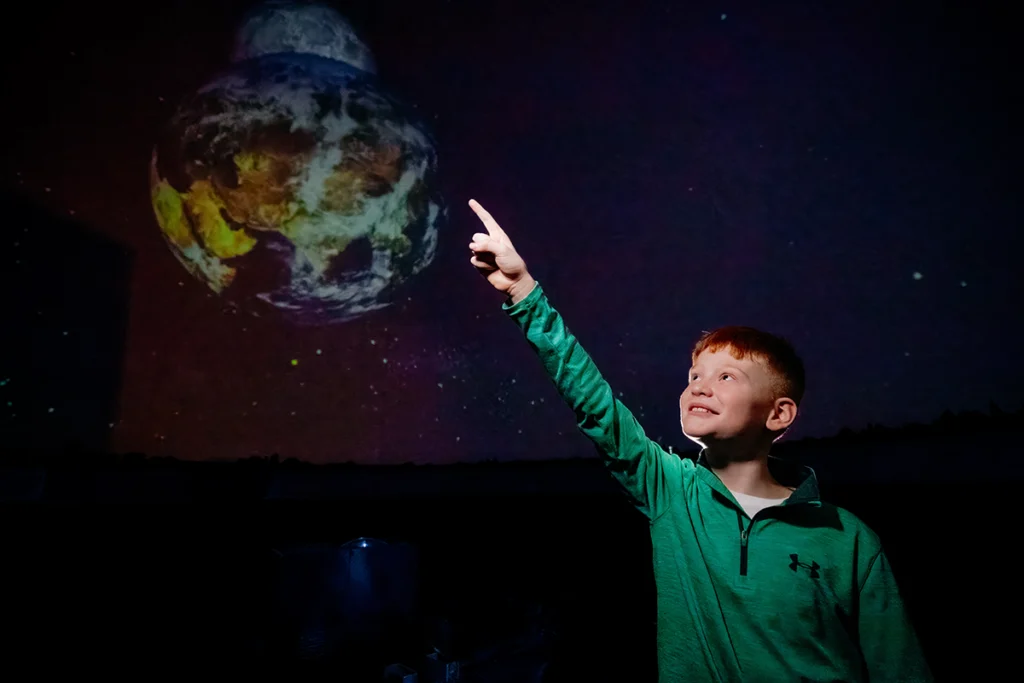 Young boy pointing at planet in sky in planetarium exhibit