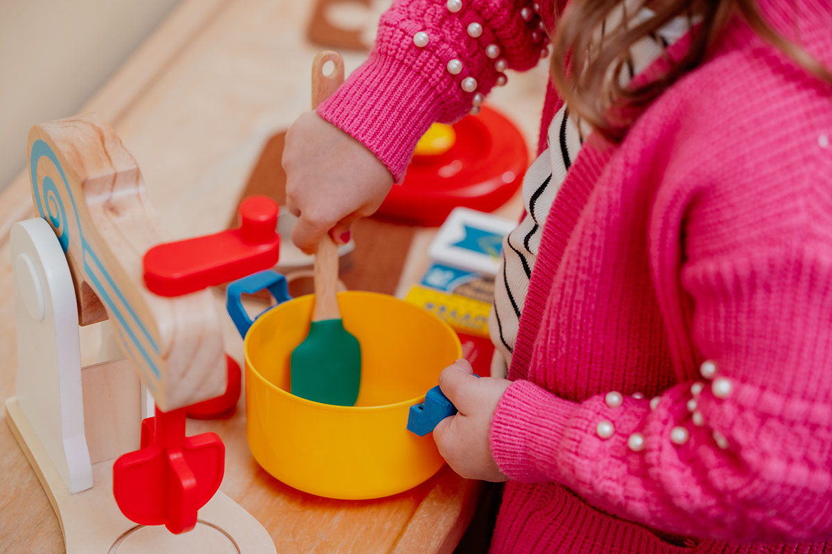 Young girl in pink sweater stirs toy pot