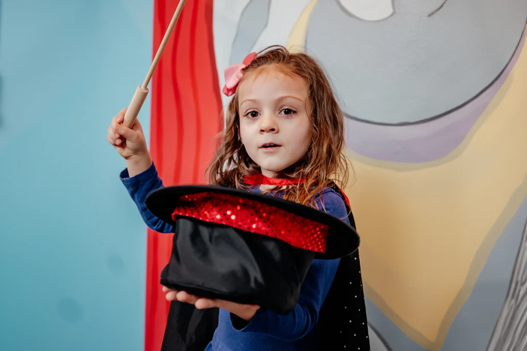 Young girl in cloak does magic trick while holding a top hat