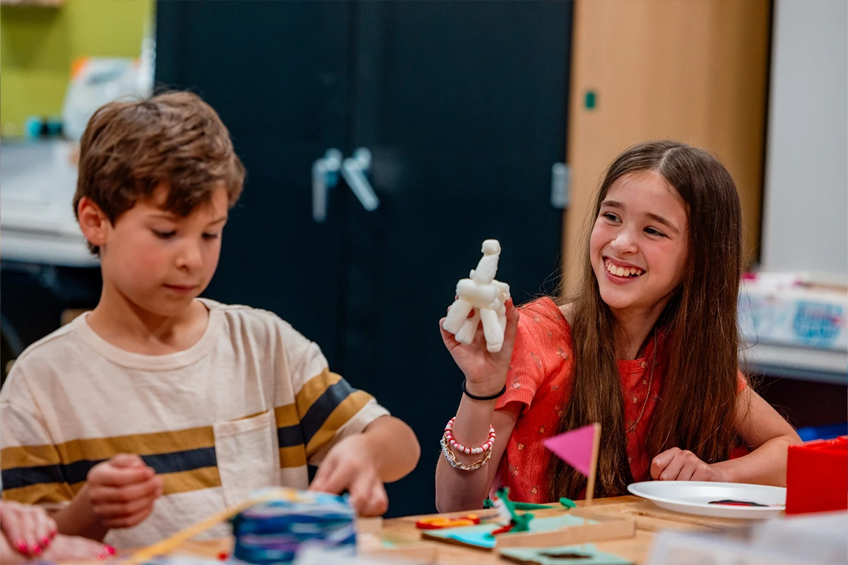 young girl shows off art piece to young boy in makerspace