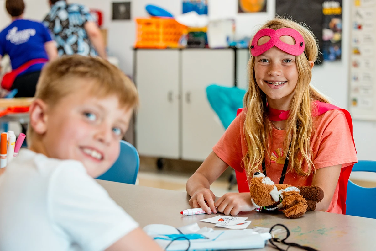 girl dressed up as superhero colors at table with young boy