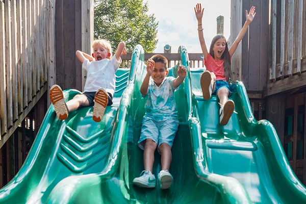 3 children sliding down slide in play area