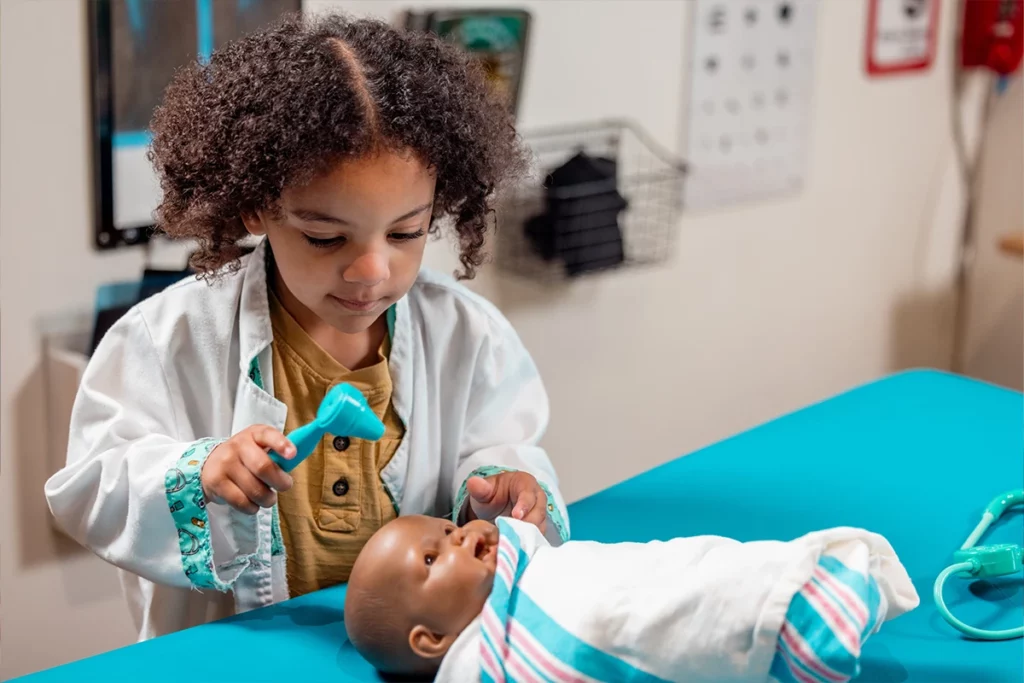 girl dressed as doctor examines baby doll